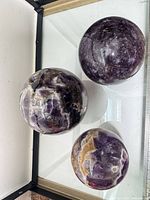 Three polished amethyst spheres with mica veins displayed in glass case