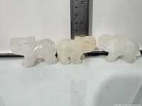 Front left view of three clear quartz elephant figurines beside ruler showing approx 2 in height