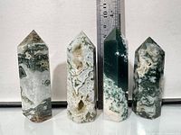 Front view of four moss agate crystal towers against ruler for scale.