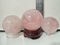 Front view of three rose quartz spheres on respective stands with ruler for scale