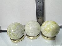 three mottled green-white stone spheres on metal stands with ruler for scale