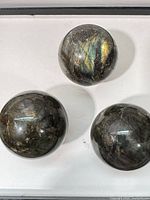 Three labradorite spheres on white background showing color flashes