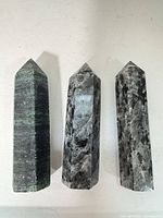 Three polished Larvikite crystal towers standing upright on a light surface