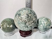 Front view of three moss agate spheres on stands with ruler for scale