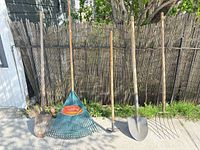 Front view of all five yard tools standing upright against fence