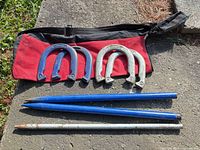 Entire horseshoe game set laid out: four horseshoes, three stakes, carry bag