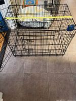 Front view of black wire dog crate showing side door, latches, and tape measure across length