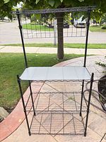 Full view of assembled black metal wire shelving unit showing three shelves and top header with plastic liner