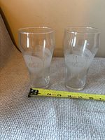 Both Coca-Cola Blockbuster 25th Celebration glasses side by side with tape measure for scale