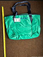 Front view of green Vulcan tote bag with tape measure for scale