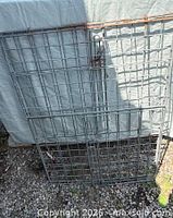 Folded metal wire kennel panels leaning against backdrop, shows grid pattern and latch