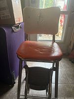 Front view of vintage chrome chair with orange seat, white backrest, fold-out black steps