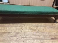 Side view of bench showing green upholstered top and wooden legs