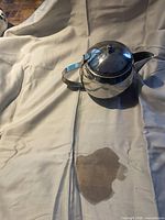 Silver-tone metal teapot on fabric backdrop