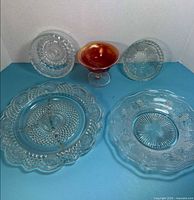 All five glass items laid out: carnival compote, pressed plates and bowls