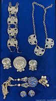 Full lot overview showing bracelet, swirl necklace, mask brooch and earrings, filigree necklace, blue rhinestone earrings