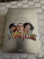 Closed metal collector’s tin showing embossed Three Stooges 75th Anniversary artwork
