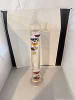 Full view of glass Galileo thermometer showing column, base, colored bulbs, and metal tags