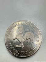 Obverse of the 1973 Codiac Dollar coin showing rooster design and inscriptions