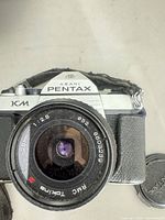 Front view of Asahi Pentax KM camera with attached RMC Tokina 28 mm lens and front lens cap beside