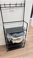 Full view of assembled black metal coat rack showing hooks and three shelves