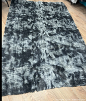 Full view of rectangular grey/black shag rug on wood floor