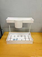 Fully assembled white L-shaped sink caddy showing lower slide-out tray, hanging cup and top tray