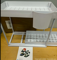 Front view of assembled white two-tier storage caddy with trays and cup, instruction sheet and box behind