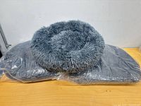 One unwrapped shaggy round pet bed resting on two identical beds sealed in plastic