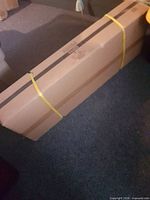 Sealed cardboard box strapped with yellow bands containing the wall mount