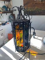Full view of wrought iron lantern on counter displaying coloured glass panels and scrolled top