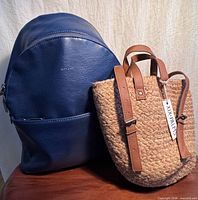 Front view of both backpacks showing Matt & Nat blue vegan leather and XIX Palms woven straw designs