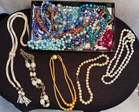 Overview of entire lot on table showing tray of assorted blue necklaces and separate necklaces outside tray
