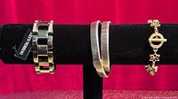 All three bracelets displayed on stand: Dyrberg/Kern link, J.Crew double coil, D’Orlan charm