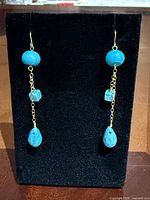Front view of both gold and turquoise drop earrings on display stand