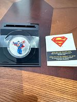 Coin in capsule on black stand next to booklet