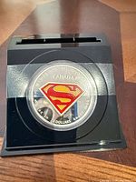 Coin in capsule inside acrylic display stand showing Superman shield reverse