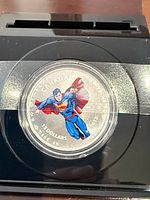 Obverse view of colored Superman coin inside capsule on black mount