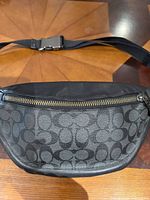 Front view of Coach belt bag showing coated canvas signature pattern, leather top panel, main zipper