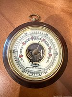 Front view of round Fisher barometer showing dial, wood frame, brass bezel
