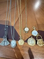 Group shot of all seven pendant watches showing variety in form, colour and chains