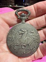 Embossed horse motif side of pocket watch with tarnish visible