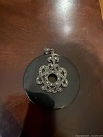 Front view showing black stone disc, silver filigree with marcasite, and bail