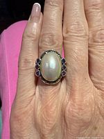 Top view of ring on hand showing mother-of-pearl center, amethyst side stones and marcasite halo
