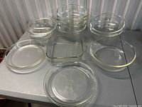 Full group view showing 12 clear Pyrex pieces: pie plates, square dish, stacked round casseroles