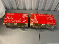 Two red cardboard four-packs each holding four clear glass Arlington punch cups