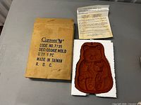 Terracotta teddy bear cookie mold resting in styrofoam next to cardboard box and instructions