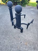 Full view of both cast iron andirons standing on pavement