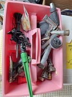 Pink caddy holding assorted hose nozzles, green spike sprinkler, brass couplings and washers