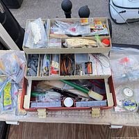 overall view of open tackle box showing trays filled with assorted tackle and additional packaged items on table